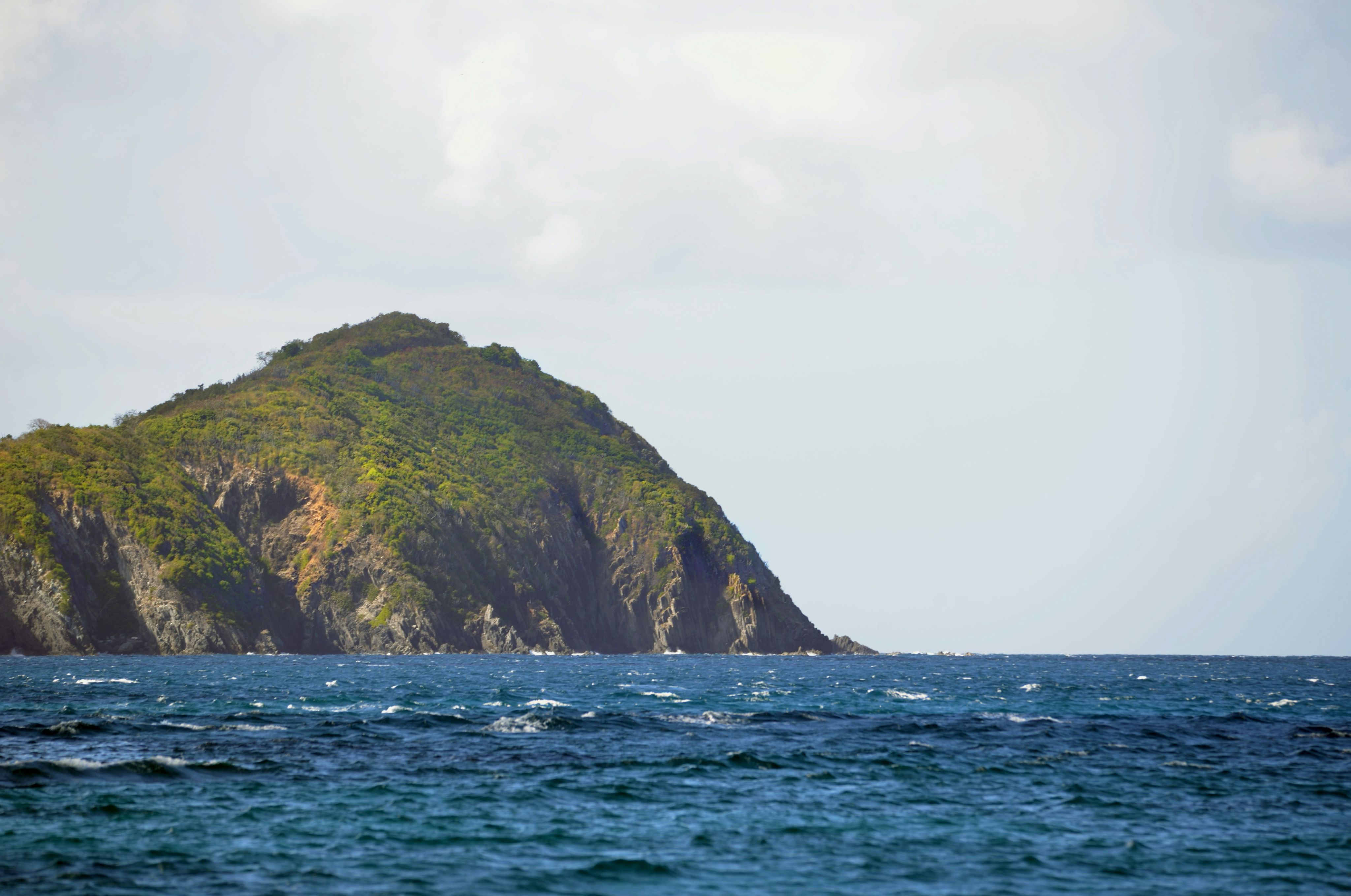 a large green cliff next to a body of water